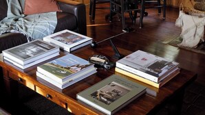 A wooden coffee table with several books, a black floor lamp, and a cozy living room setting with a sofa and chairs. - The Writer's Cabin in Lake Arrowhead Woods (Lake Arrowhead)
