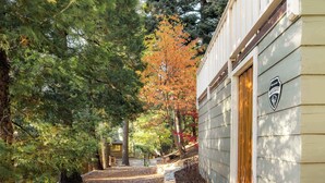 A pathway leading to a building with a security sign, surrounded by trees with autumn foliage. - The Writer's Cabin in Lake Arrowhead Woods (Lake Arrowhead)