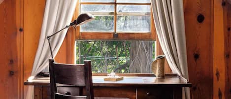 A wooden room with a sloped ceiling, a desk with a chair, and a window with curtains.