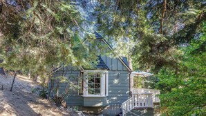 A house with a small porch, surrounded by dense trees and a dirt path leading to the entrance. - The Writer's Cabin in Lake Arrowhead Woods (Lake Arrowhead)