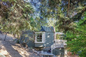 Ein Haus mit einer kleinen Veranda, umgeben von dichten Bäumen und einem Feldweg, der zum Eingang führt.