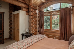 Ein Holzblockhaus-Interieur mit einem Bett, einer Holztür und einem Fenster mit Vorhängen.