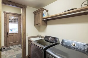 A laundry room with a front-loading washer and dryer, wooden cabinets, and a shelf above the dryer. - Luxury Mountain Village Retreat | Panoramic Mountain Views | Private Hot Tub | Sleeps 10 (Telluride)
