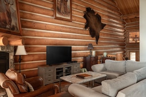Ein rustikales Blockhaus-Interieur mit Fernseher, Ledermöbeln, einem aufgehängten Tierfell und einem Kamin.