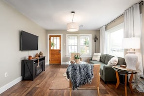 A living room with a sofa, a television, a wooden cabinet, a dining table, and a large window with curtains. - Cozy, Clean, 2-bedroom 1 bathroom home in Lexington, TN (Lexington)