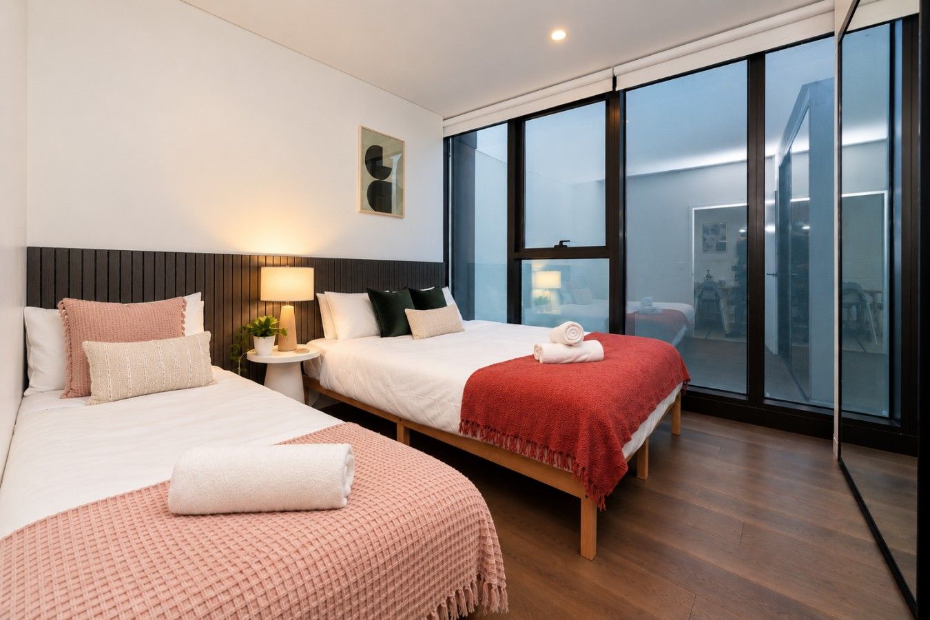 Une chambre d’hôtel avec deux lits, une table de chevet avec une lampe, une grande fenêtre donnant sur un beau paysage et un plancher en bois.