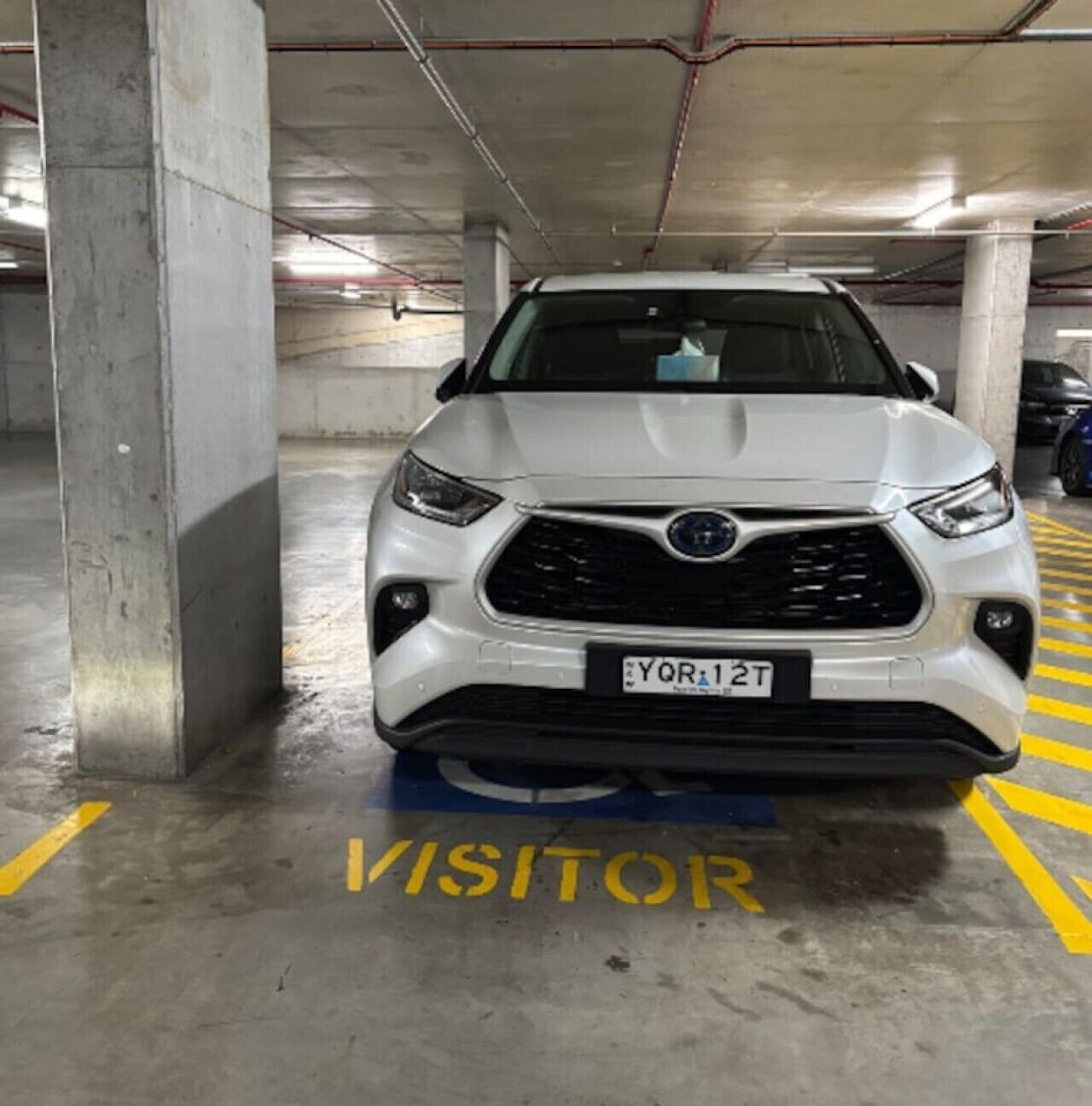 Un VUS blanc était stationné sur une place de stationnement réservée aux visiteurs, à proximité d’un pilier en béton.