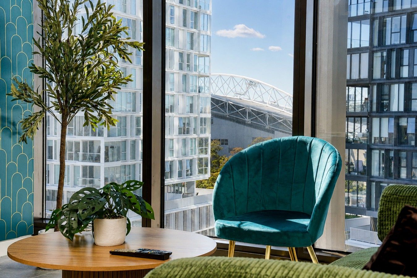 Un intérieur moderne avec un fauteuil recouvert d’un tissu de couleur turquoise, une table ronde en bois et une plante en pot.