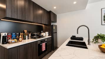 Kitchen corner showing the four burner gas cooktop on the bench against the wall with the oven below it, dark cabinetry with a marble look benchtop, and under cabinet lighting. The island sink and its gooseneck tap are in the foreground.