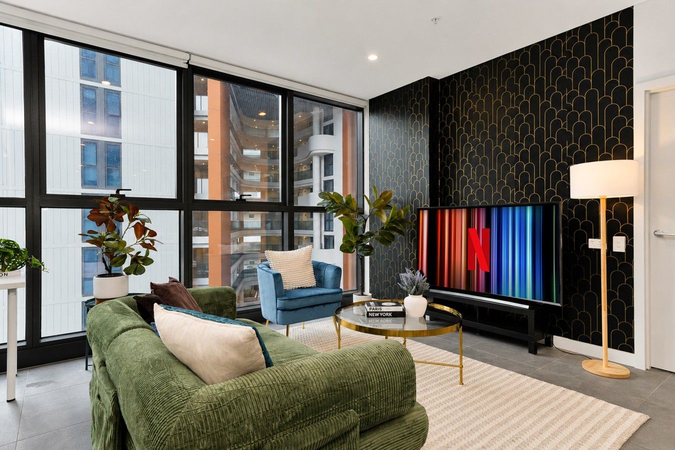 Un salon moderne avec un canapé vert, un fauteuil bleu et un grand écran de télévision affichant le logo de Netflix.