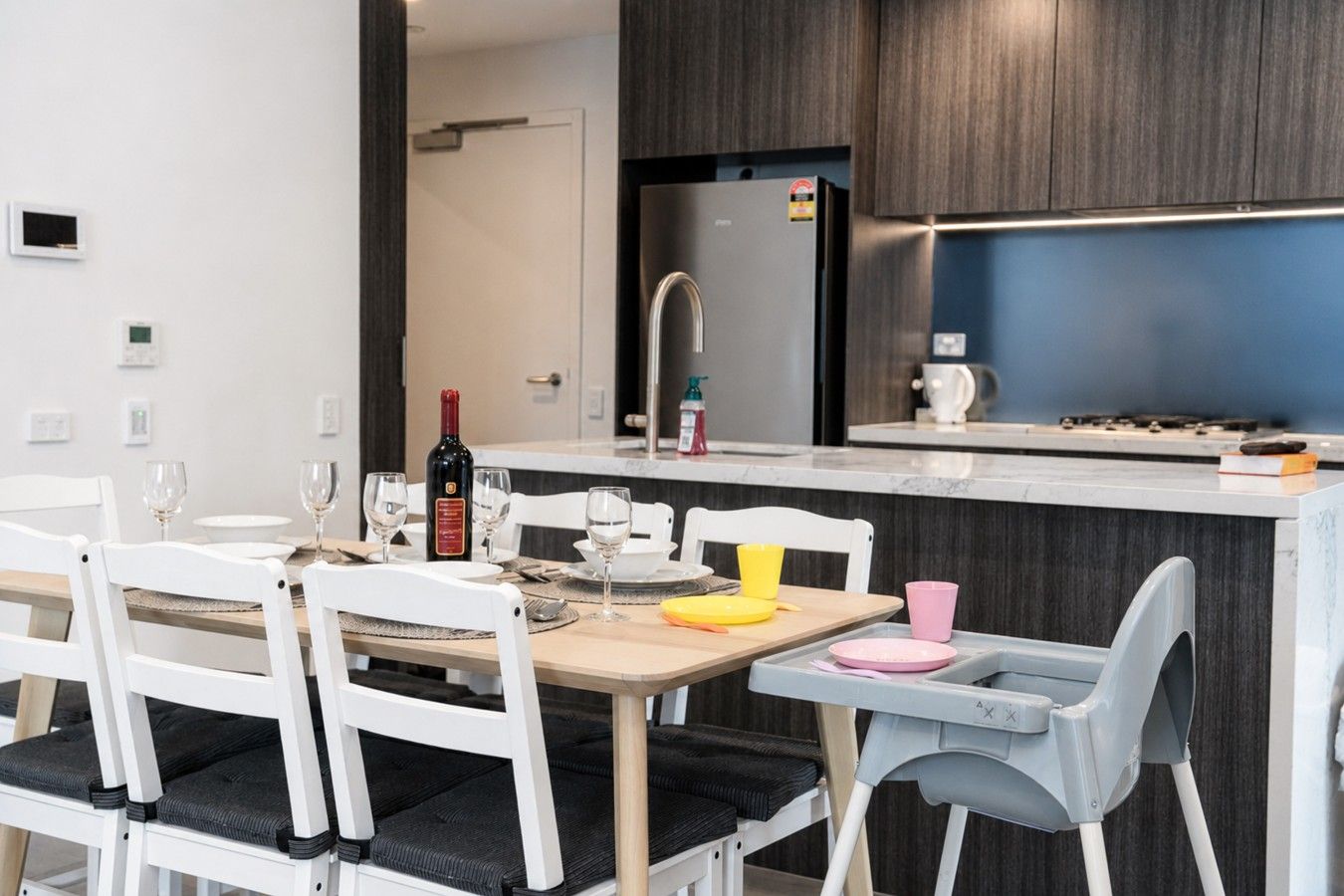 A modern kitchen with a central island, white chairs, and a dining table set for two.
