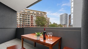 Un balcon avec une table en bois, deux verres à vin et une bouteille de vin.