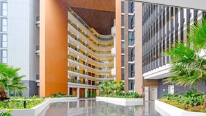 Un atrium à plusieurs niveaux, doté d’un espace central ouvert, entouré de bâtiments modernes avec des balcons et des revêtements de sol réfléchissants.