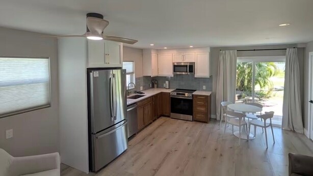 A modern kitchen with stainless steel appliances, wooden cabinets, and a dining area with a table and chairs. - The Eden (Fort Myers Beach)