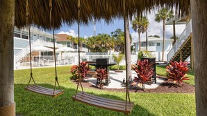 A covered outdoor area with a swing set, a grill, and a pool. - The Eden (Fort Myers Beach)
