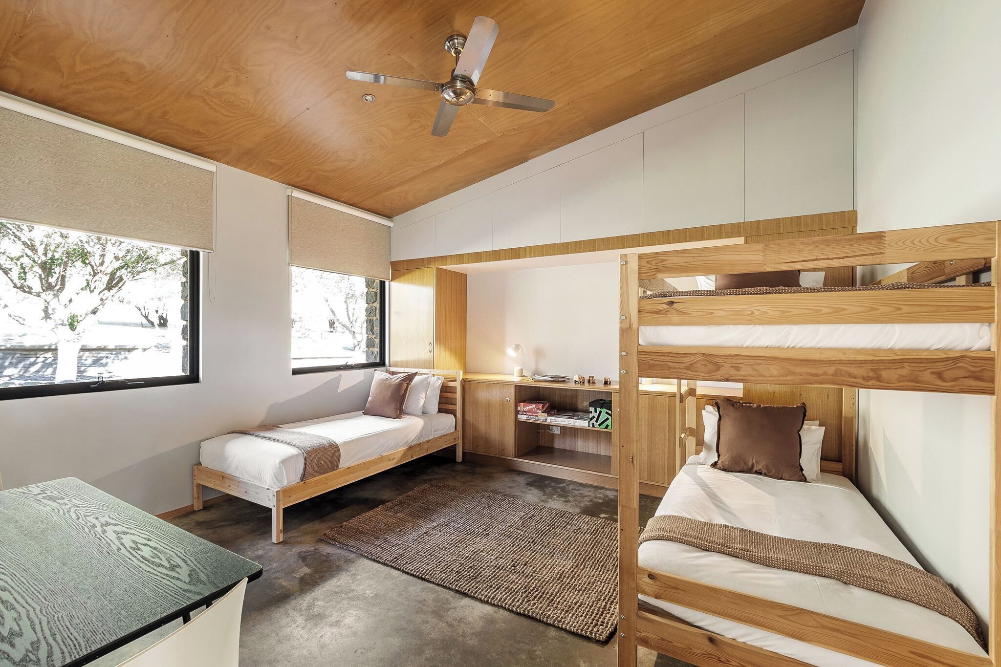 A modern bedroom with bunk beds, a desk, and a ceiling fan.