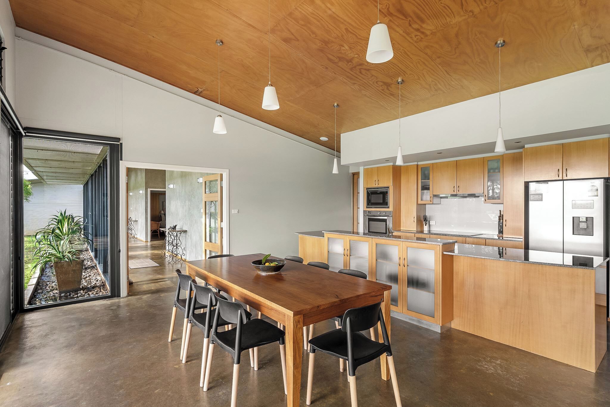 A modern kitchen with wooden cabinets, stainless steel appliances, and a dining area with a wooden table and chairs.