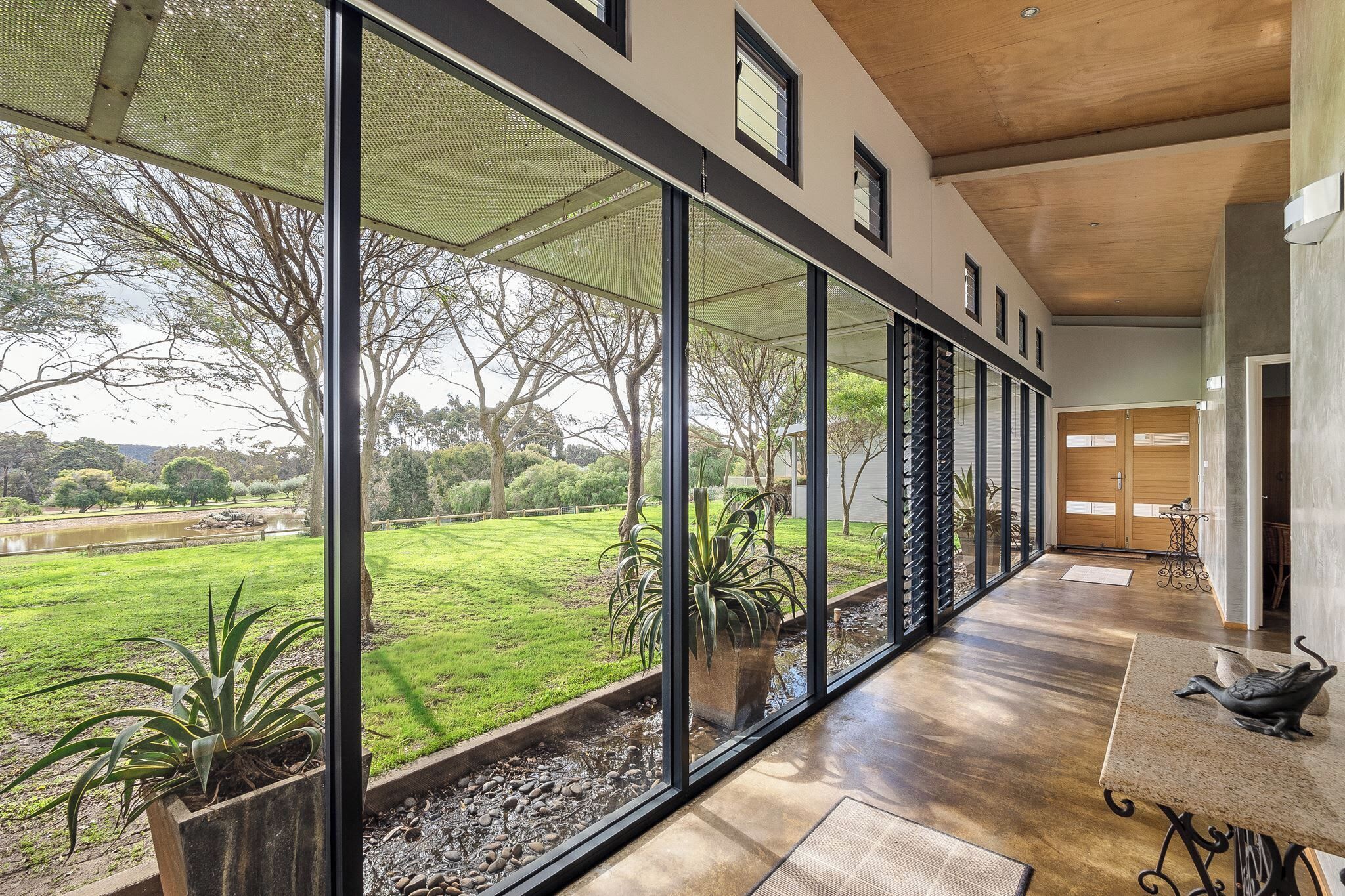 A corridor with large windows, a view of a grassy area, and a wooden floor.
