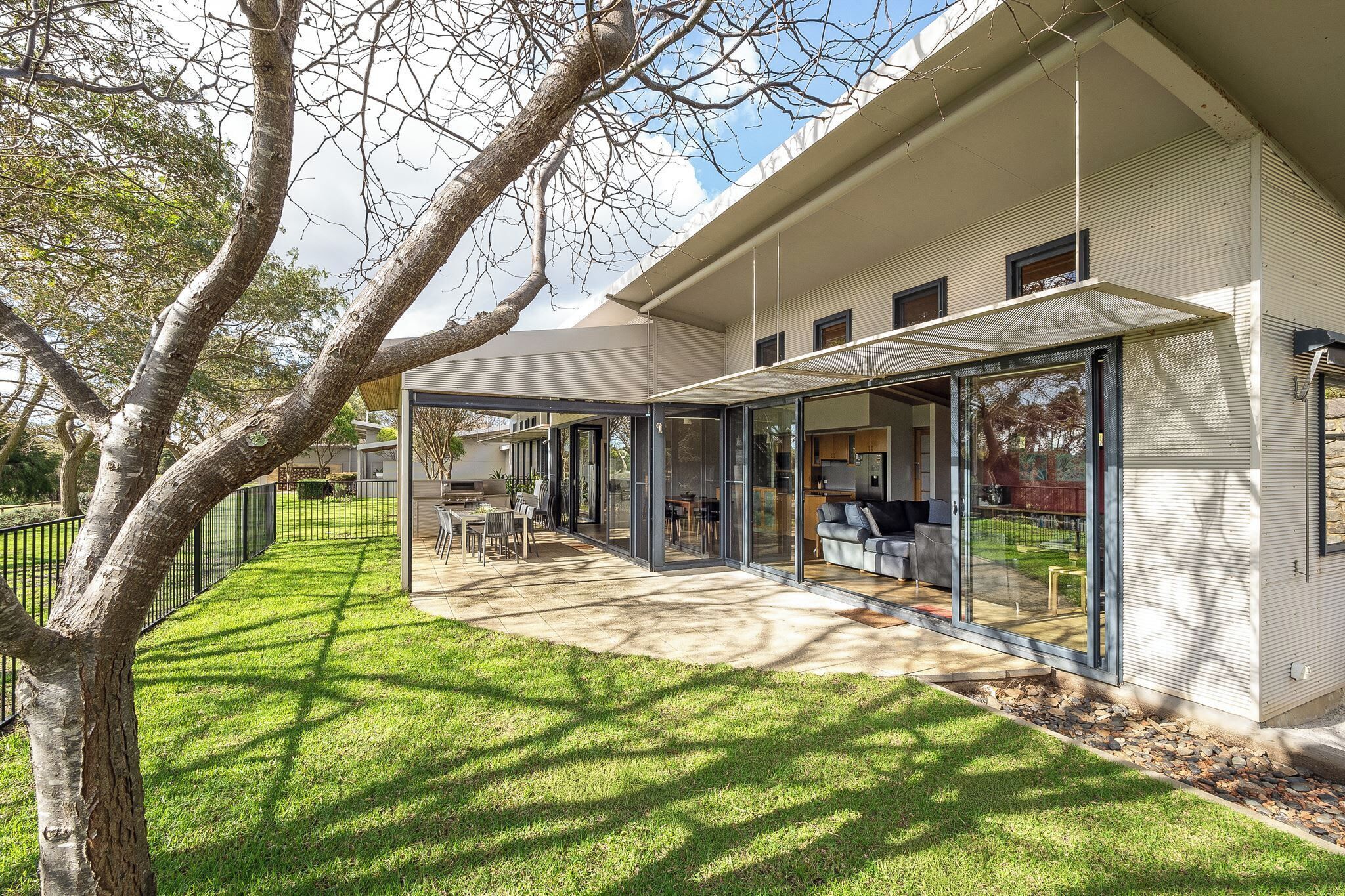 A modern house with a covered patio, a lawn, and a tree.