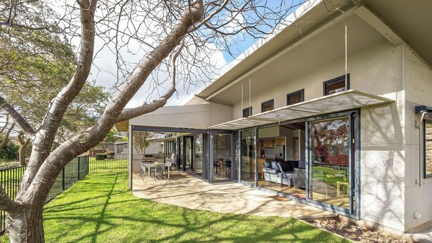 Una casa moderna con un portico coperto, un prato e un albero.