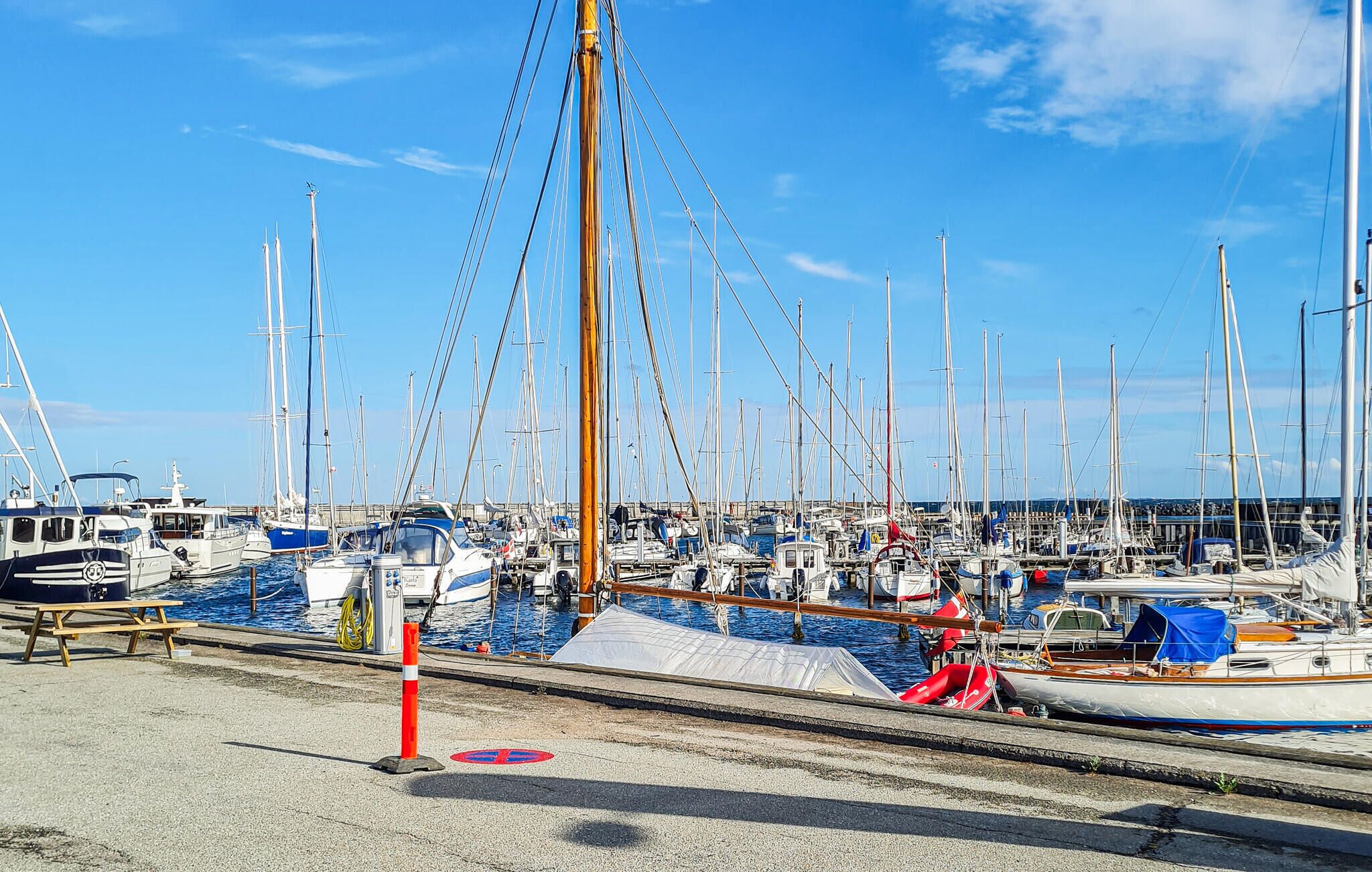 Een jachthaven met diverse zeilboten die aanmeren, een picknicktafel en een reddingsboei op de steiger.