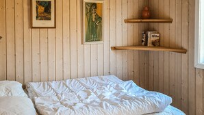 Et værelse med en seng, to billeder hængt på væggen og en reol med bøger.