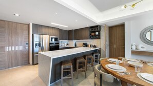 Uma cozinha moderna com uma ilha central, banquetas de bar, uma mesa de jantar posta para quatro e eletrodomésticos embutidos.