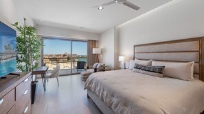 Ein modernes Hotelzimmer mit einem großen Bett, einem Fernseher, einem Balkon mit Blick auf den Strand und einem Essbereich.
