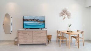 Ein modernes Zimmer mit Flachbildfernseher auf einem Holzschrank, einem Esstisch mit Stühlen und einer dekorativen Wandgestalt.