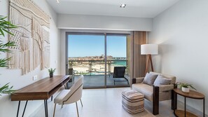Ein modernes Wohnzimmer mit einem großen Schiebeglasfenster, das auf einen Balkon mit Blick auf Strand und Stadt führt.