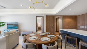 Een moderne eetruimte met een ronde tafel voor zes personen, een bank en een televisie waarop een kustlandschap te zien is.