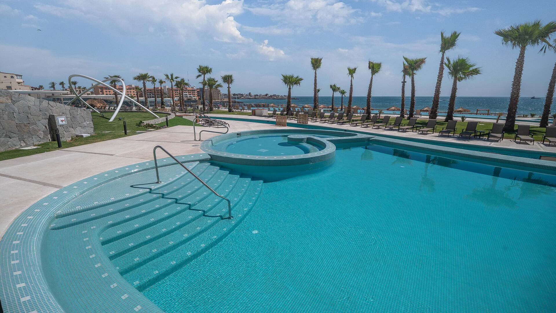 Une piscine avec un jacuzzi circulaire, entourée de palmiers et de chaises longues.