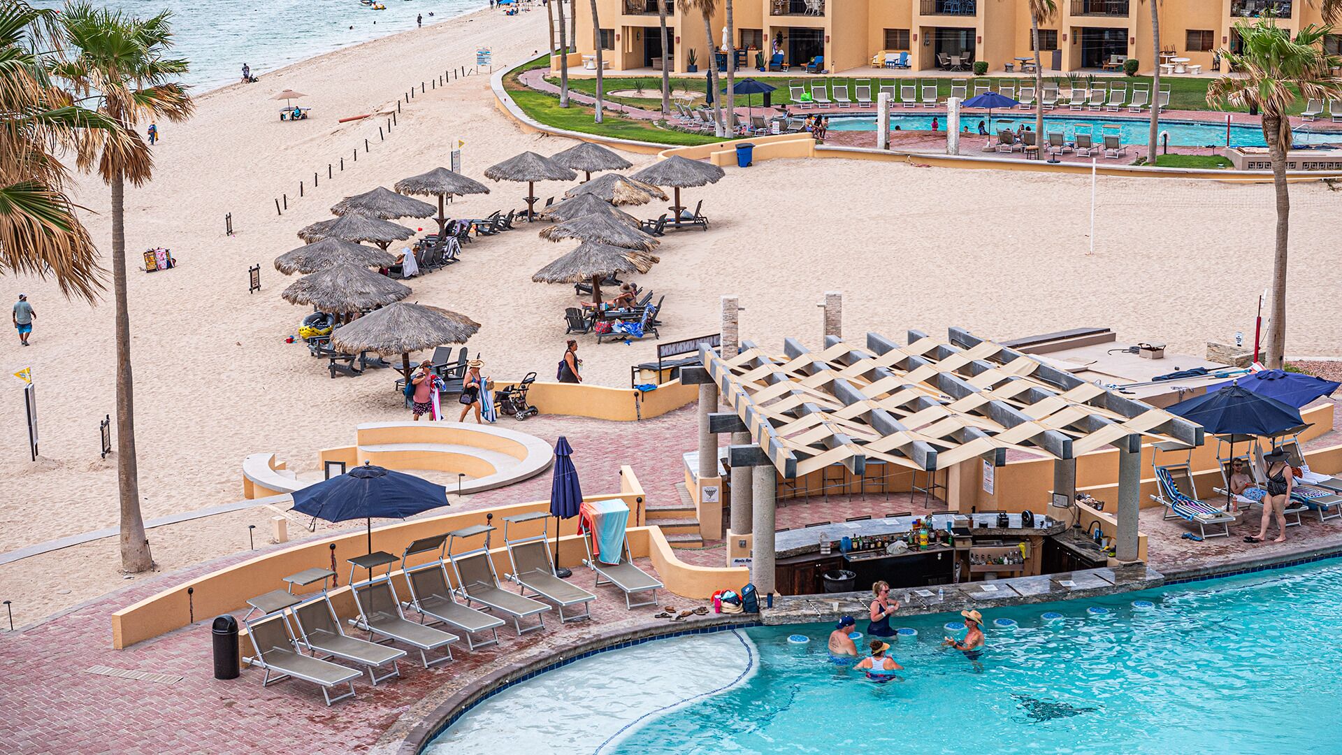 A resort with a pool area, beach, and lounge chairs.