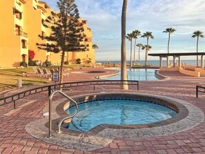 A hotel pool area with a heated pool, palm trees, and a view of the ocean. - Oceanfront 2BR Condo at Princesa Resort with Stunning Sea of Cortez Views (Puerto Peñasco)