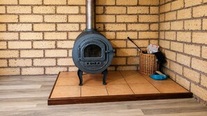 A wood-burning stove with a metal chimney, a wicker basket, and a blue basin on a tiled floor. - Yelverton Brook - Jarrah Lodge - 2 bedroom (Metricup)