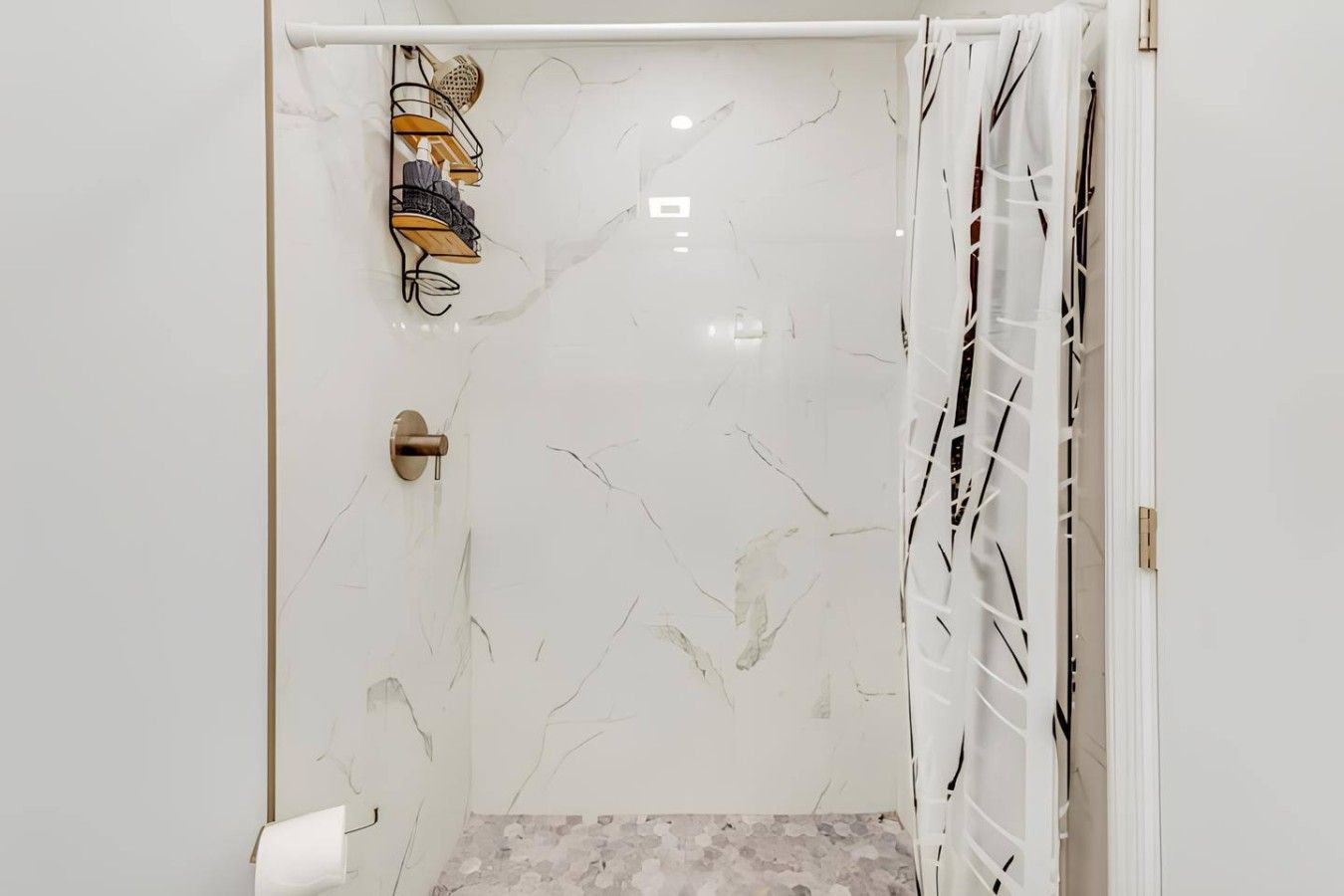 A bathroom with a white marble wall, a shower with a white curtain, and a towel rack with multiple towels.