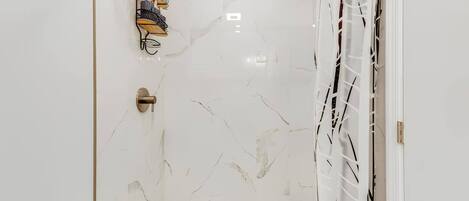 A bathroom with a white marble wall, a shower with a white curtain, and a towel rack with multiple towels.