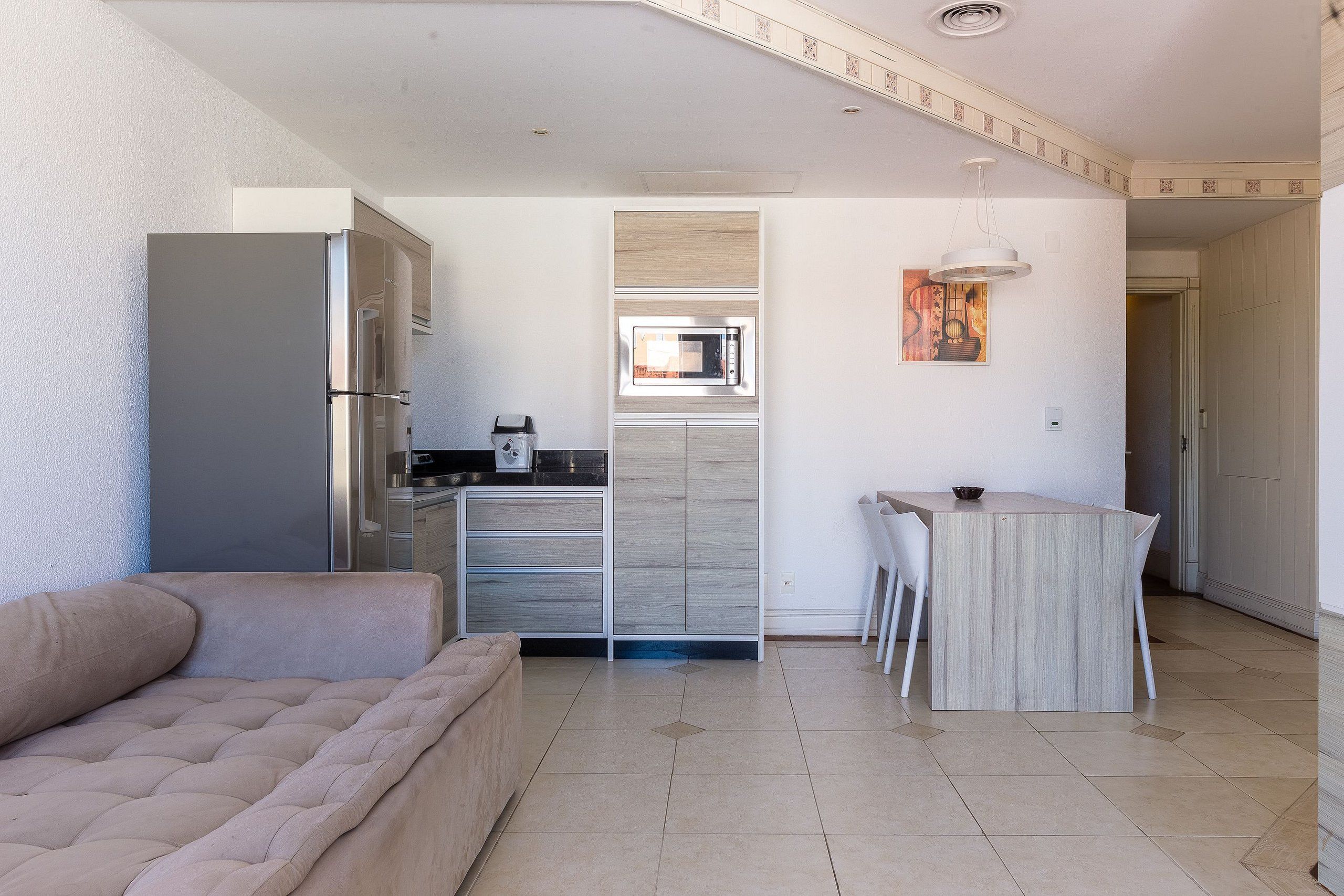 A modern kitchen with a built-in microwave, a dining area with a small table and chairs, and a beige sofa in a living area.