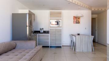 A modern kitchen with a built-in microwave, a dining area with a small table and chairs, and a beige sofa in a living area.