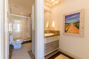 A bathroom with a shower, toilet, sink, and a painting of a beach scene. - Luxury Penthouse W/sea View Jurere Resort Ilc1506 (Florianópolis)
