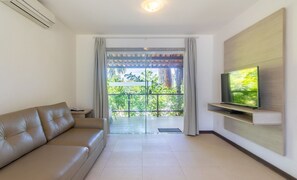Ein modernes Wohnzimmer mit einer Ledersofa, einem flachbildfernseher an der Wand und einer Glasschiebetür, die auf einen mit Grünwerk bedeckten Balkon führt.