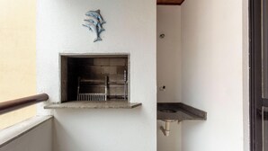 A small, enclosed grill area with a metal grate, a stone shelf, and a wall-mounted fish decoration. - Comfortable Ap 80m Praia dos Ingleses Amc0202 (Florianópolis)