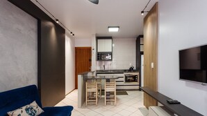 A modern kitchen with a TV, a dining area with chairs, and a blue sofa. - Comfortable Ap 80m Praia dos Ingleses Amc0202 (Florianópolis)