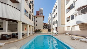 A swimming pool surrounded by white buildings with balconies, a clear sky, and lounge chairs. - Comfortable Ap 80m Praia dos Ingleses Amc0202 (Florianópolis)