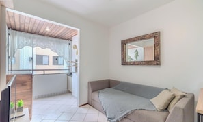 A living room with a sofa, a mirror, and a view of a balcony with a house. - Belo Cozy Apartment 4 Minutes From the sea Amc0204 (Florianópolis)