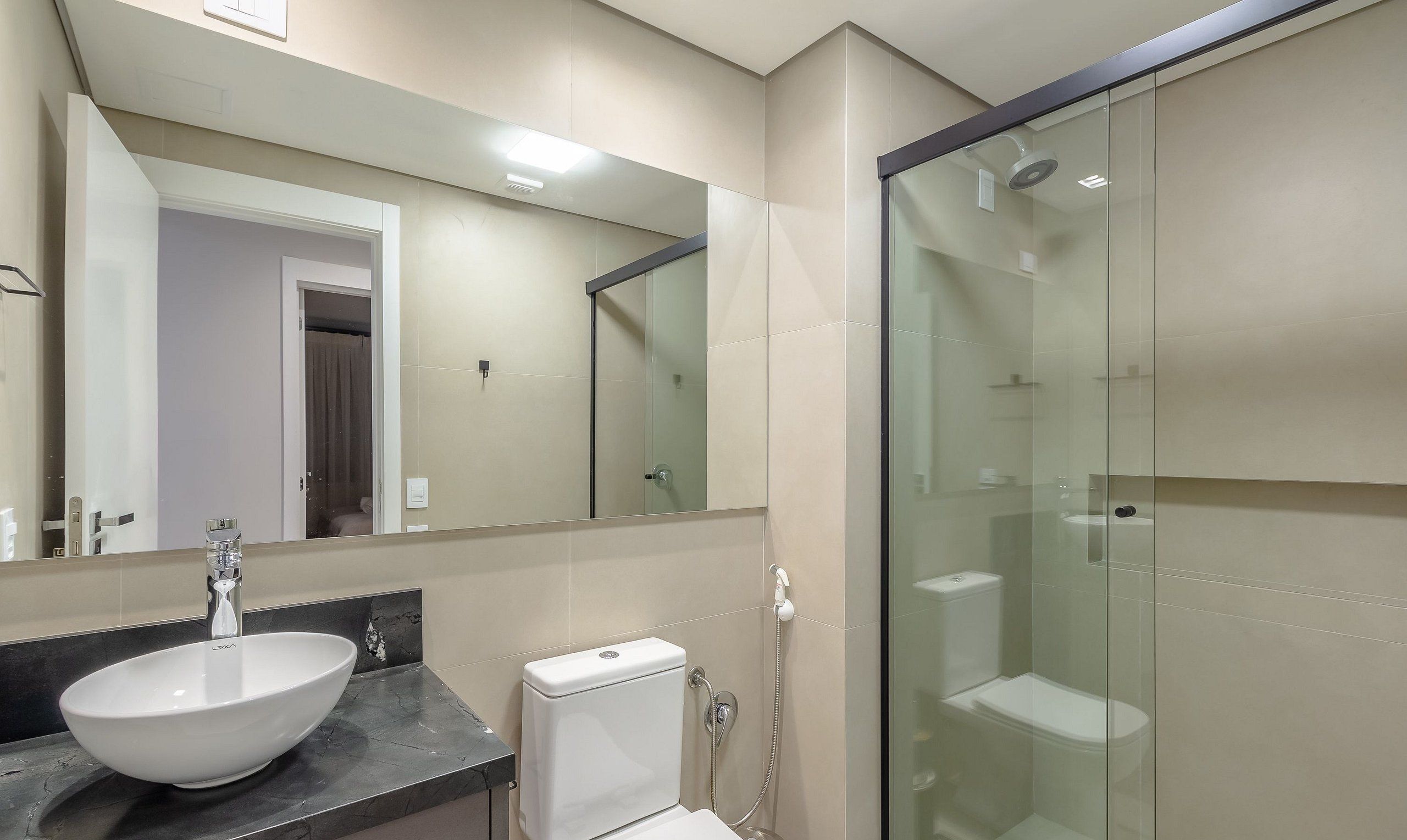 A modern bathroom with a large mirror, a sink, a toilet, and a glass-enclosed shower.