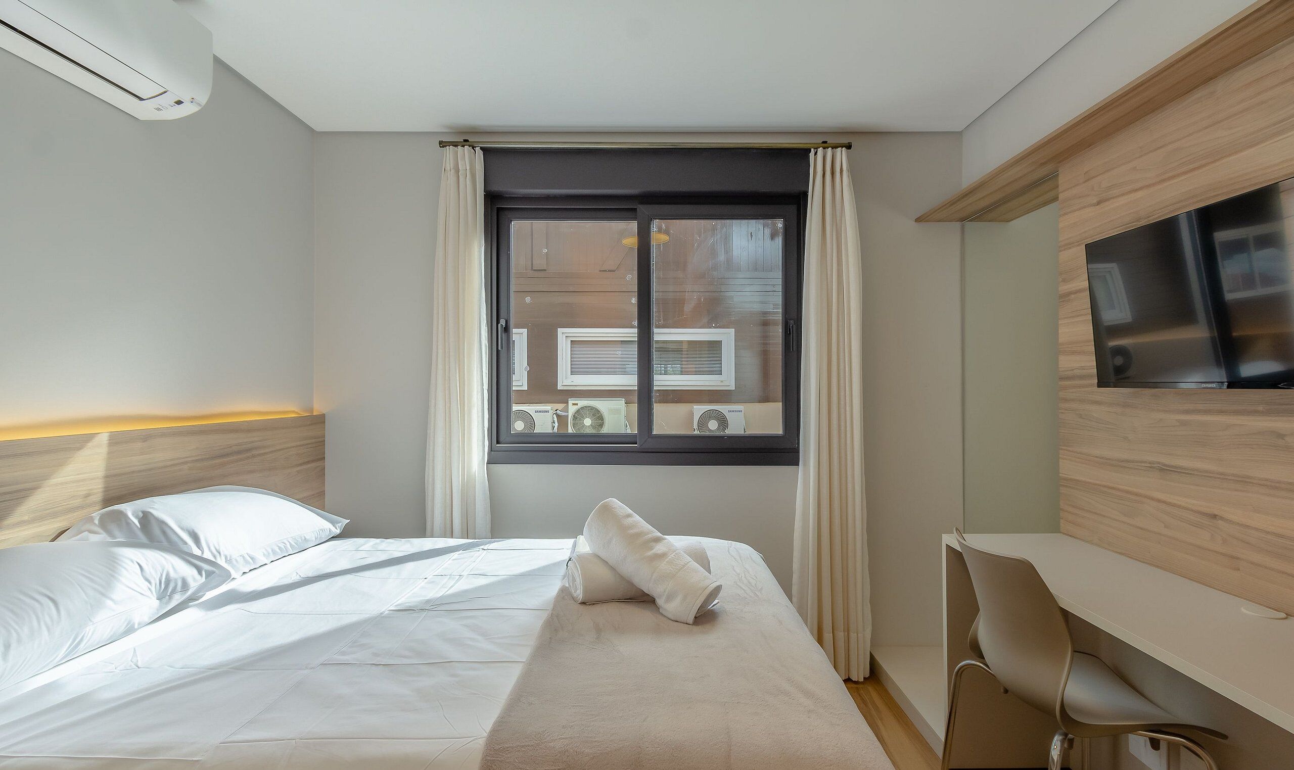 Habitación de hotel con cama, escritorio, silla, ventana con cortinas y equipo de aire acondicionado.