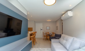 A modern living room with a flat-screen TV, a sofa, a dining table with chairs, and a kitchen area in the background. - Cozy Apartment in Downtown Gramado Dlh0302 (Gramado)