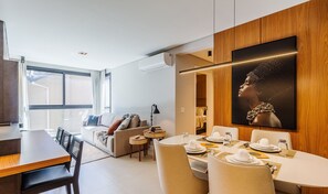 A modern living room with a dining area, a large window, and a wall-mounted artwork. - Apartment in the Center Near Rua Coberta Dlh0303 (Gramado)