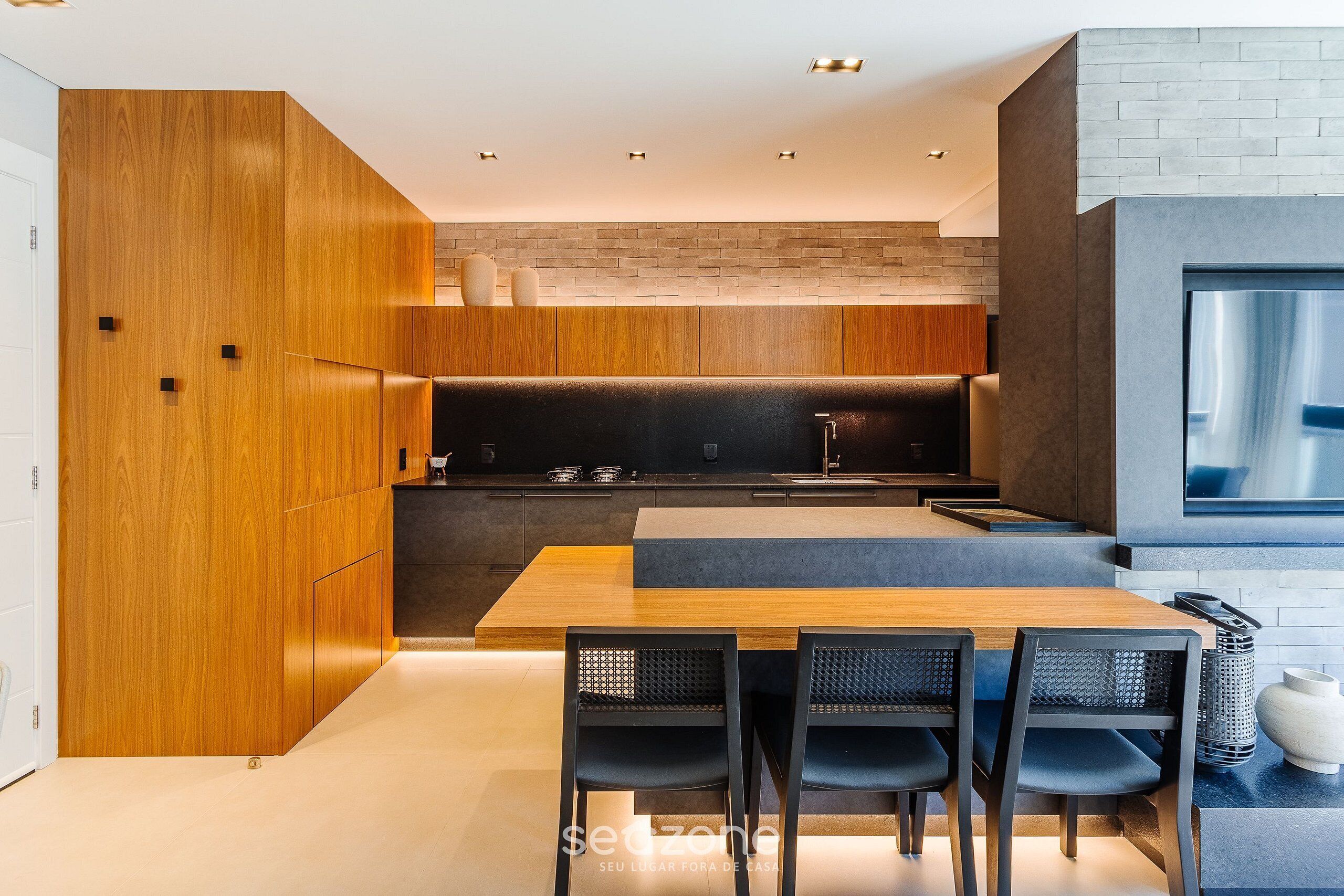 Una cocina moderna con armarios de madera, encimera negra y zona de comedor con cuatro sillas.